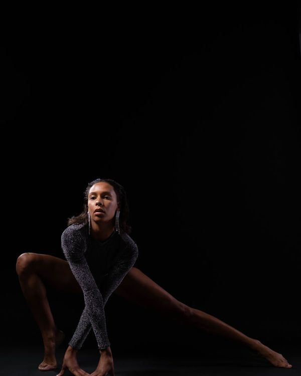 Woman in a dynamic yoga pose against a dark background with accent light.